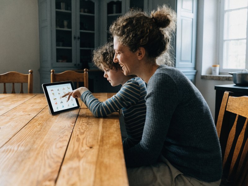 A parent and child at the kitchen table looking at the app together on a tablet.